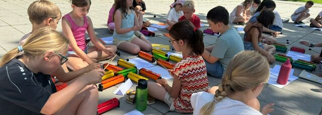 Schüler sitzen in Gruppen auf dem Boden und musizieren